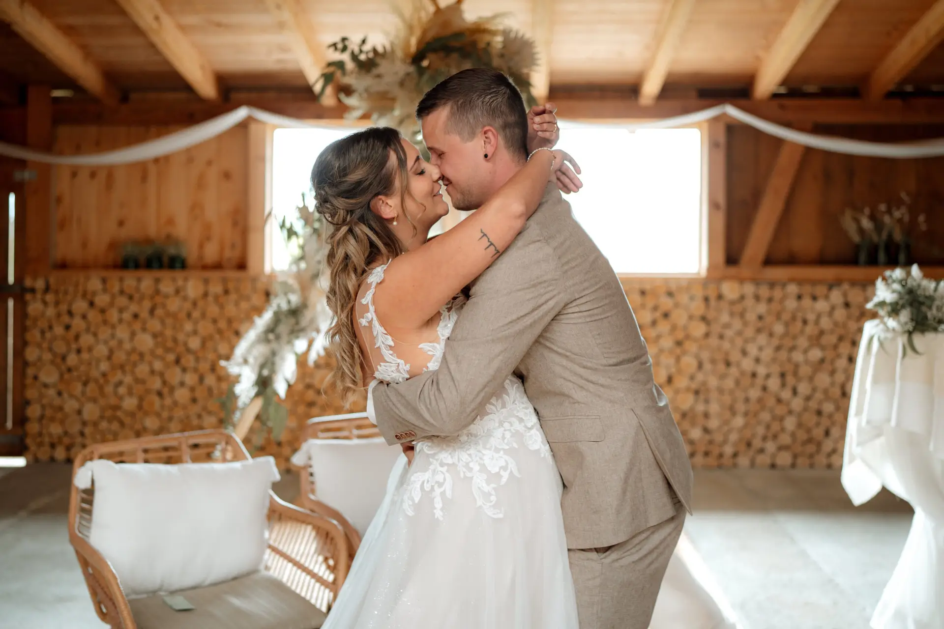 Eine Braut und ein Bräutigam umarmen sich und lächeln sich an während ihrer Hochzeit in einem rustikalen, holzgetäfelten Lokal in Luzern, wunderschön dekoriert mit weißen Blumen und drapierten Stoffen - eingefangen durch authentische hochzeitsfotografie.